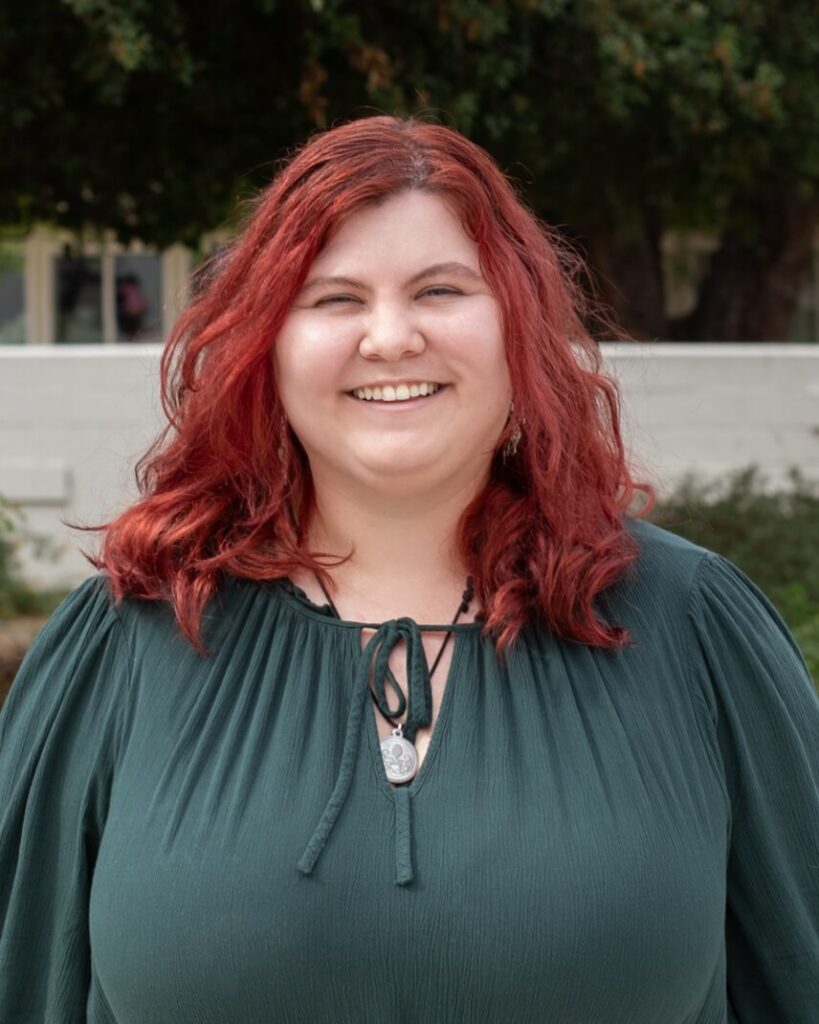 A person with long red hair wearing a green shirt.