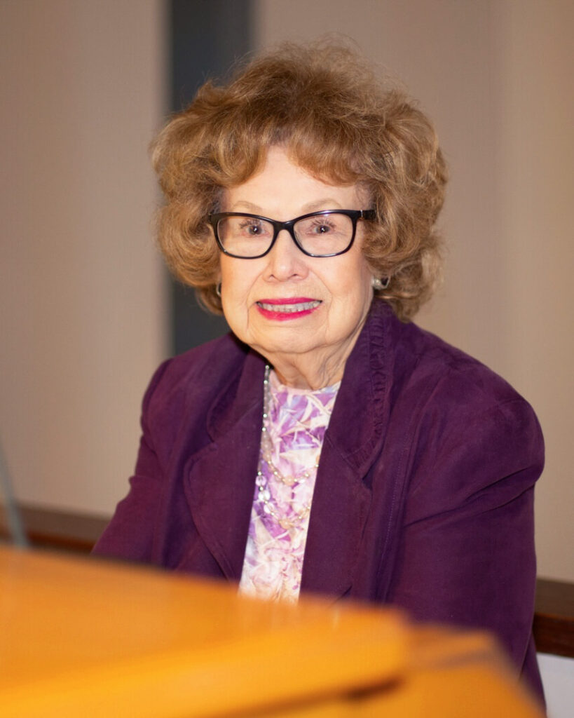 A person smiling wearing black glasses and purple jacket.