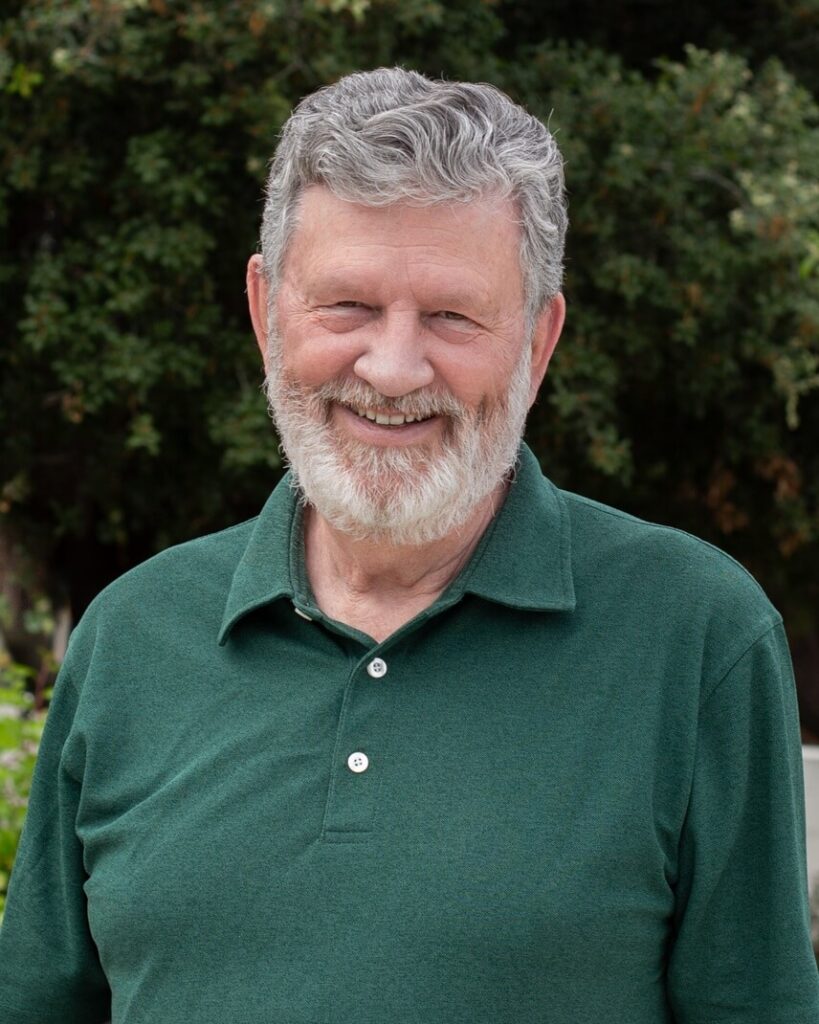 A person with short grey hair and beard smiling wearing a green polo shirt.