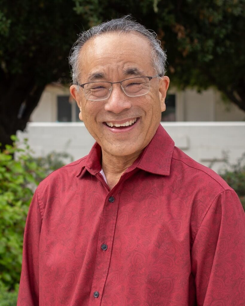 A person with short grey hair waring glasses and smiling.