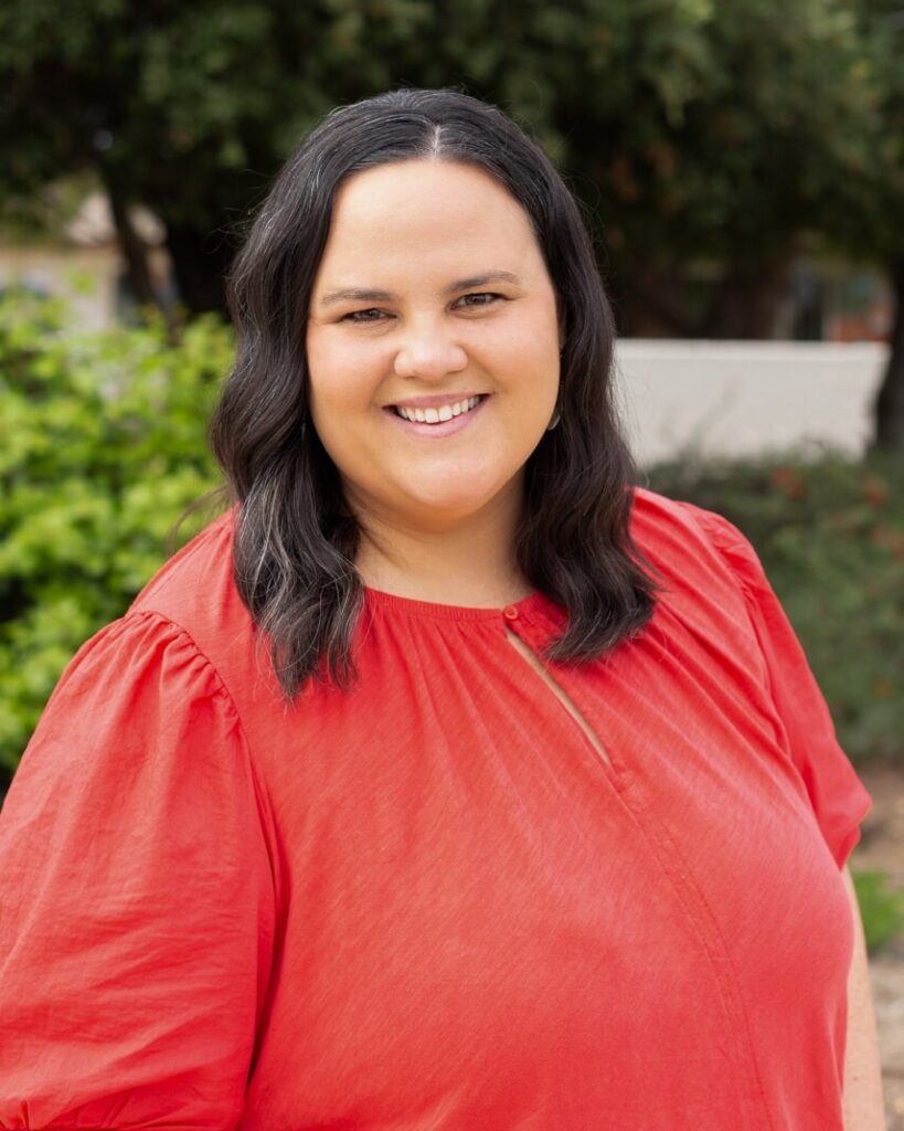 A person with long black hair smiling wearing a red shirt.